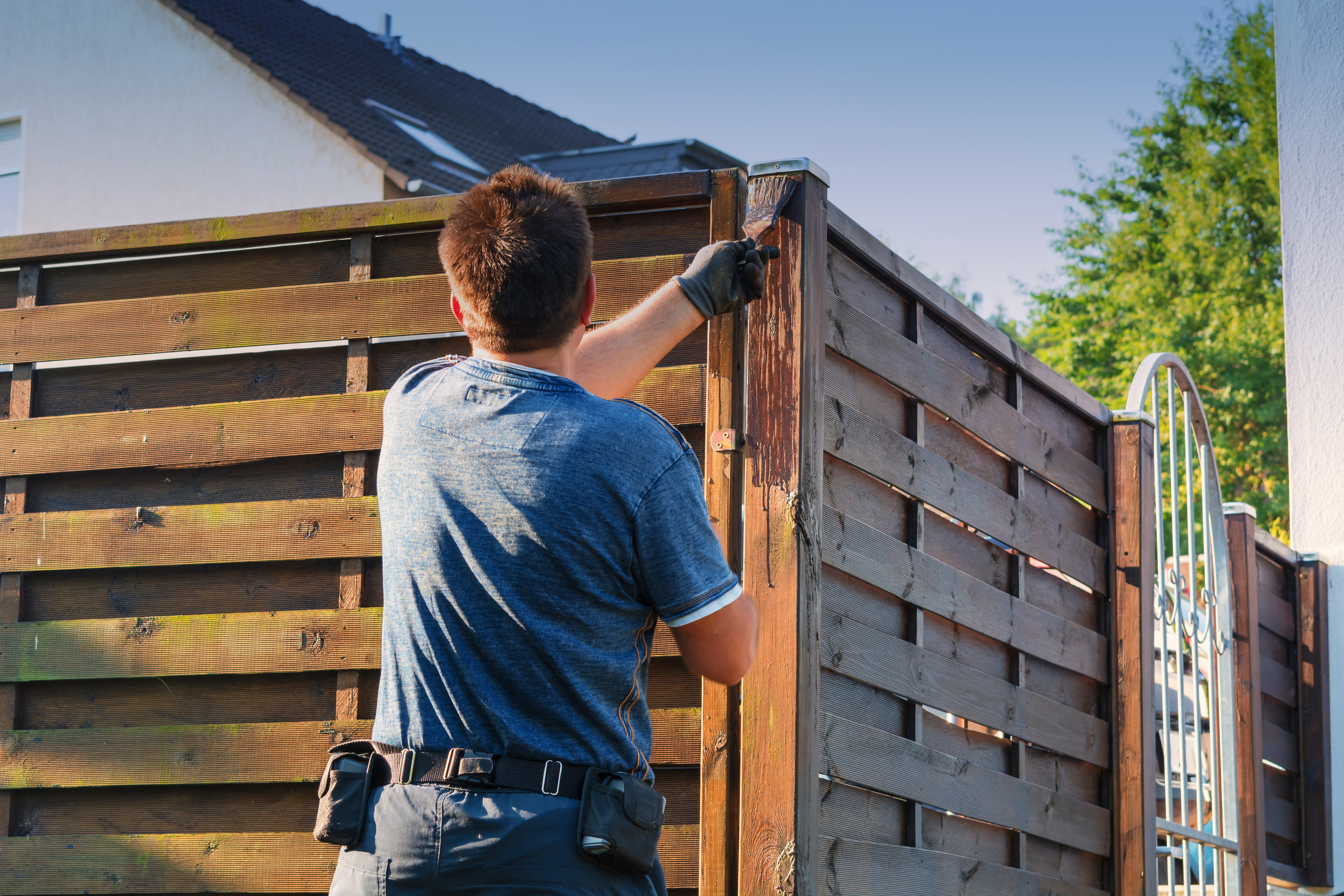 A contractor staining a wooden privacy fence, ensuring long-lasting exterior protection for coastal homes in Southeastern North Carolina.