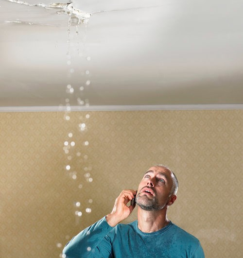 A homeowner looking up at a leaking ceiling, urgently needing roof repair services for storm damage in Southeastern North Carolina.
